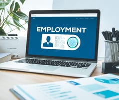 A computer sitting on a desk with a text reading "employment" on the screen